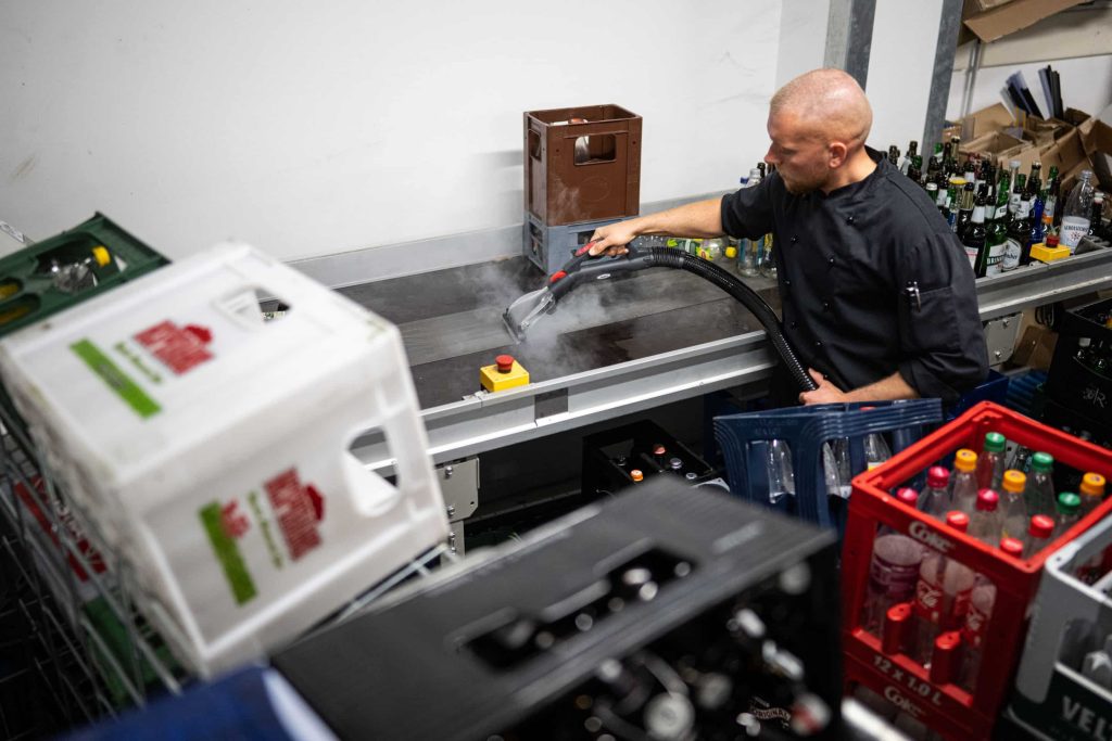 Klebrige Getränkereste auf dem Transportband müssen in der Leergutabteilung nicht sein. Sie werden mit Hilfe von Trockendampf gelöst. Foto: Lukas Schulze/beam.